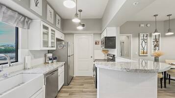 A modern kitchen with white cabinetry, a marble countertop, and pendant lighting.