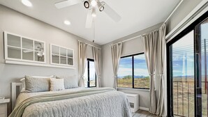 A bedroom with a large bed, a ceiling fan, a window with curtains, and a view of the outdoors. - Saguaro #202 Fountain Hills (Fountain Hills)