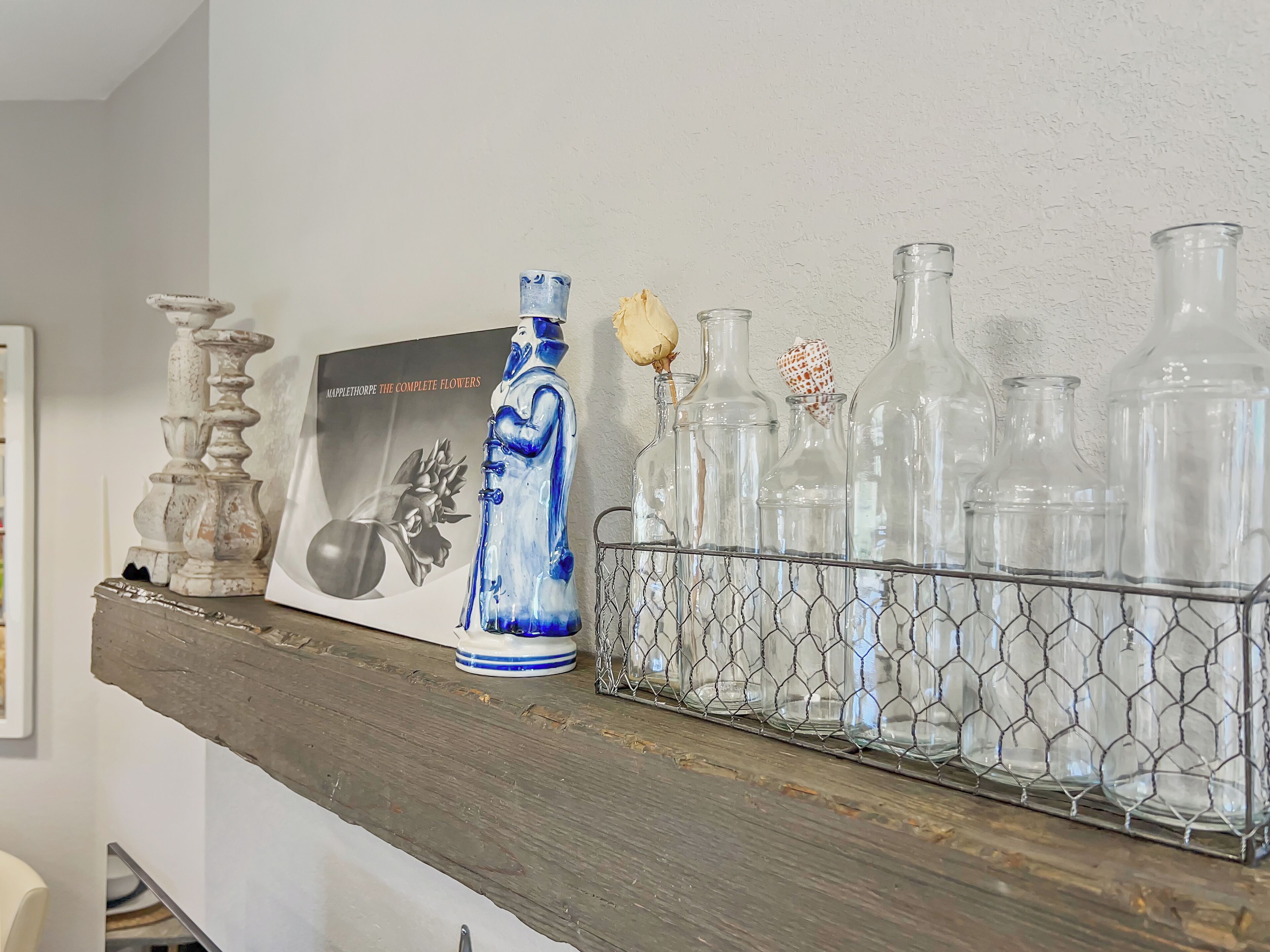 A shelf with decorative items including a blue vase, a framed picture, and a wire basket holding clear glass bottles.