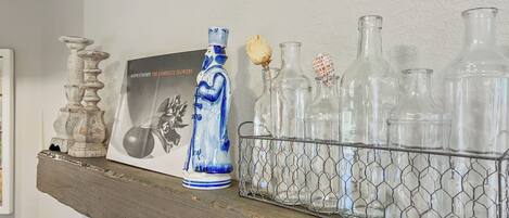 A shelf with decorative items including a blue vase, a framed picture, and a wire basket holding clear glass bottles.