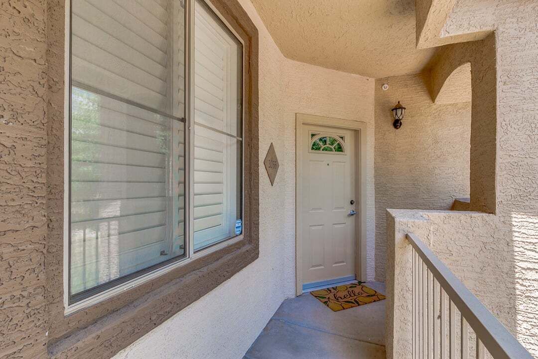 A hallway with a white door, a window with blinds, and a small rug with a 'hello' message.