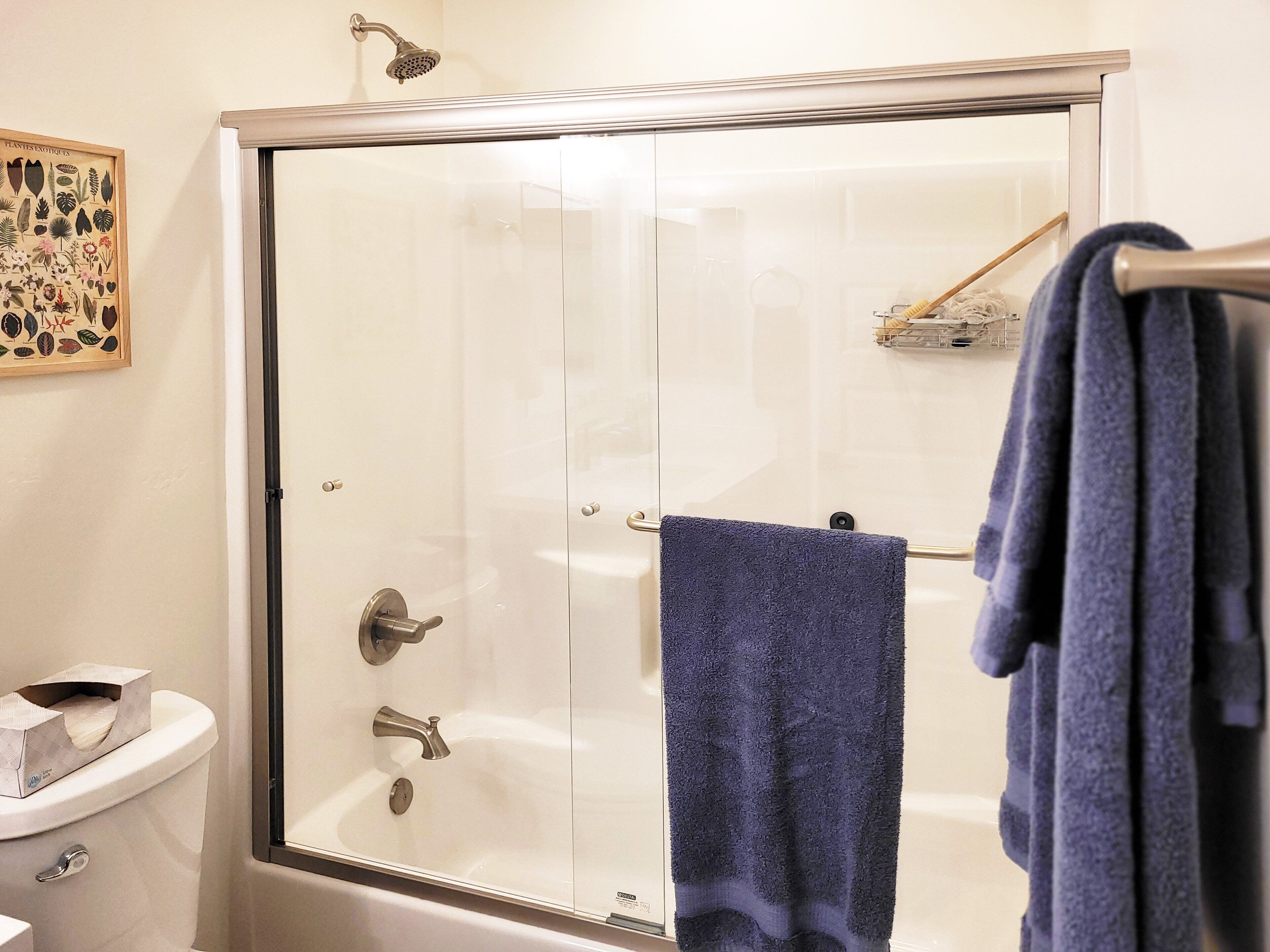 Eine begehbare Dusche mit Glaswänden, eine weiße Toilette und ein blaues Handtuch an einem Ablagekorb.