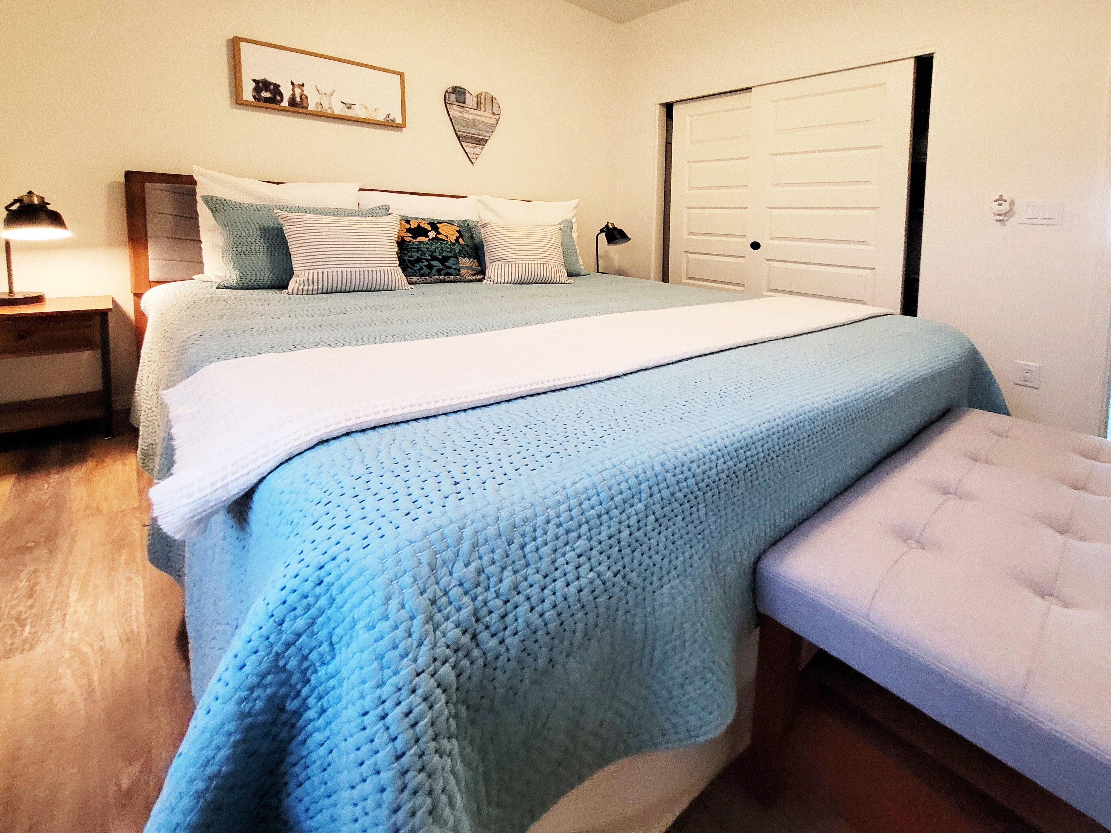 A bedroom with a large bed, a bedside table, a lamp, and a door.