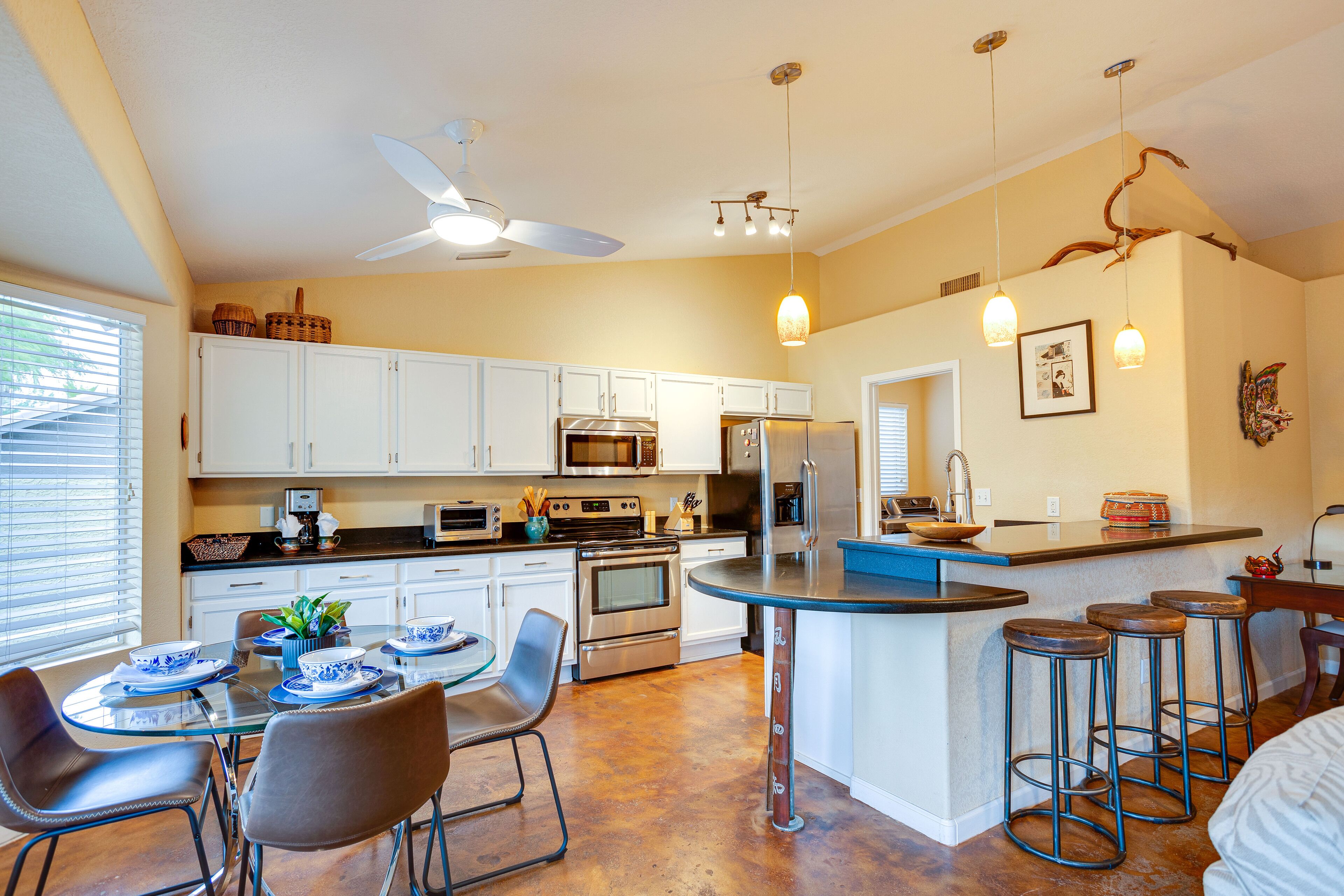A modern kitchen with white cabinets, stainless steel appliances, a dining area with a glass table, and a bar area with stools.