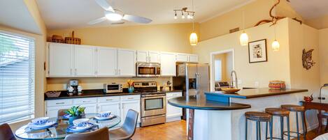 A modern kitchen with white cabinets, stainless steel appliances, a dining area with a glass table, and a bar area with stools.