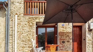 A stone building with a wooden balcony, a table with chairs, and an umbrella.