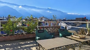 Terraza en la azotea con vistas a montañas, plantas en macetas y una mesa.
