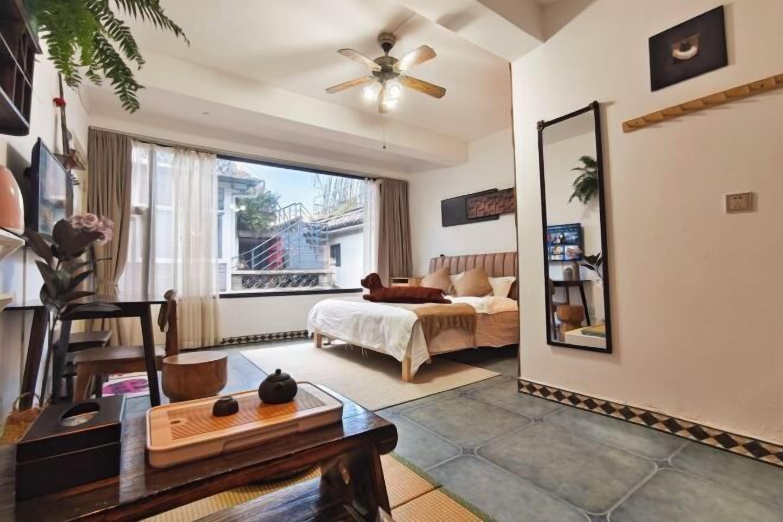 Un dormitorio con una cama, ventilador de techo, ventana y espejo en la pared.