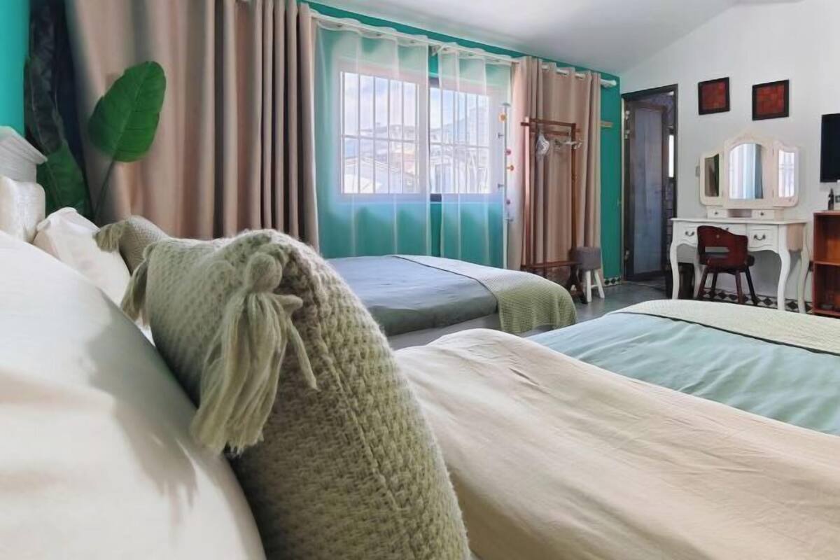 Une chambre d’hôtel avec deux lits, un bureau, une chaise, un miroir et une fenêtre avec des rideaux.