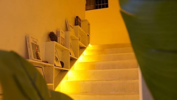 Una escalera con luz cálida en la parte inferior, rodeada de estanterías y una decoración con piña.