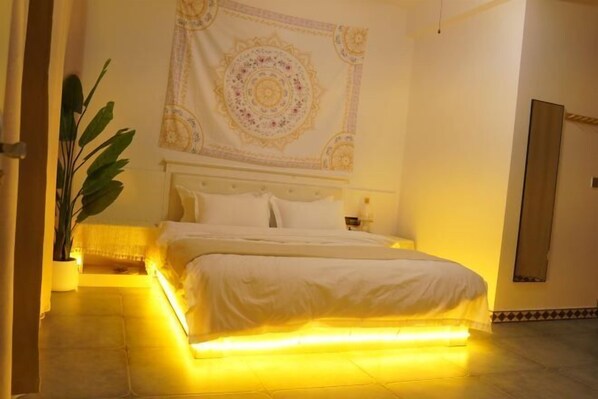 A bedroom with a bed, a large tapestry on the wall, and a potted plant. - Walking Flowers Inn (Dali City)