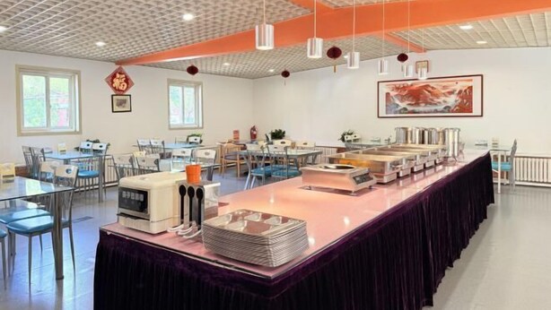 Une pièce spacieuse avec une longue table dressée pour le repas, de nombreuses chaises et un plafond orné d’un motif en réseau.