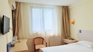 Une chambre d’hôtel comprenant un lit, un bureau avec une chaise, une télévision, une fenêtre avec des rideaux, un radiateur et un téléphone fixé au mur.