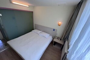 A hotel room with a bed, bedside table, lamp, and a window with curtains. - Hejia Hotel (Beijing niujieGuang'anmen Hospital of Traditional Chinese Medicine) (Beijing)