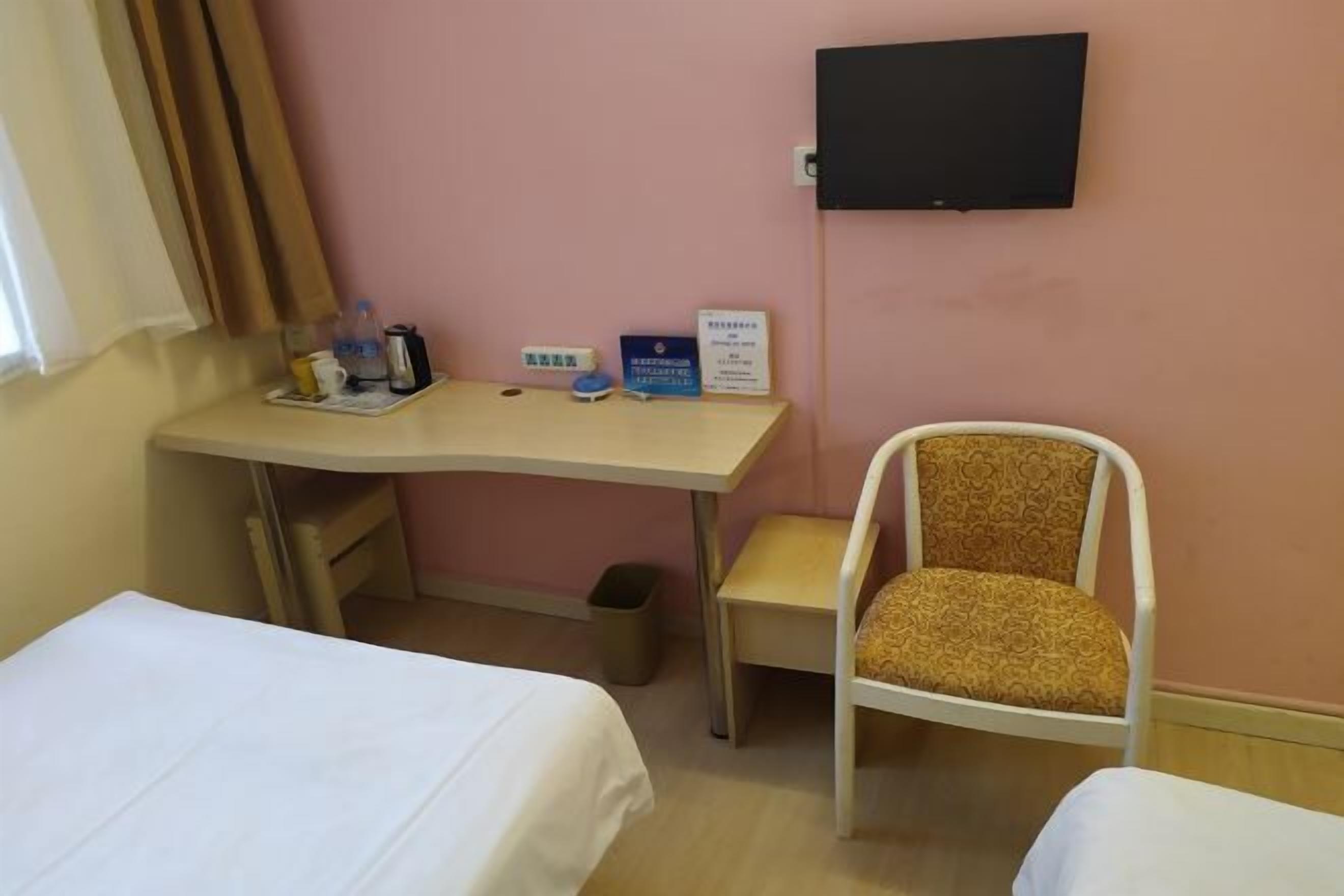 Ett hotellrum med en säng, ett skrivbord, en stol och en tv på väggen.
