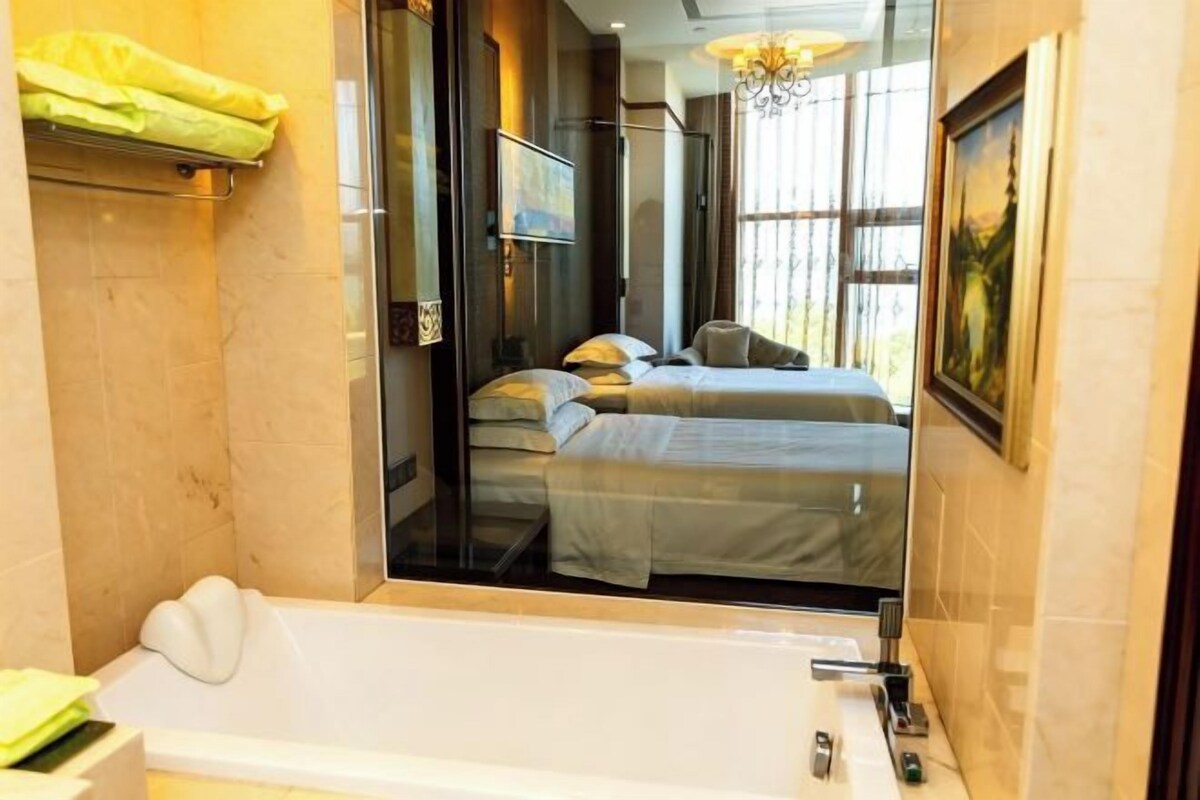 A hotel room with a large mirror, a bathtub, and a bed with two pillows.