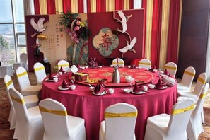 A round table with a red tablecloth, white chairs with yellow sashes, and a decorative backdrop with white doves and Chinese characters. - Wei Select Xueye Hotel (Jinan)