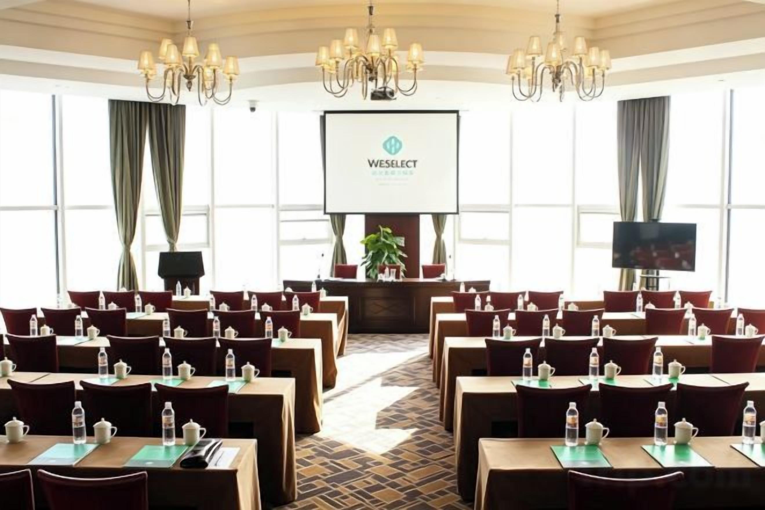 A conference room with rows of tables and chairs, a projector screen, and a television.