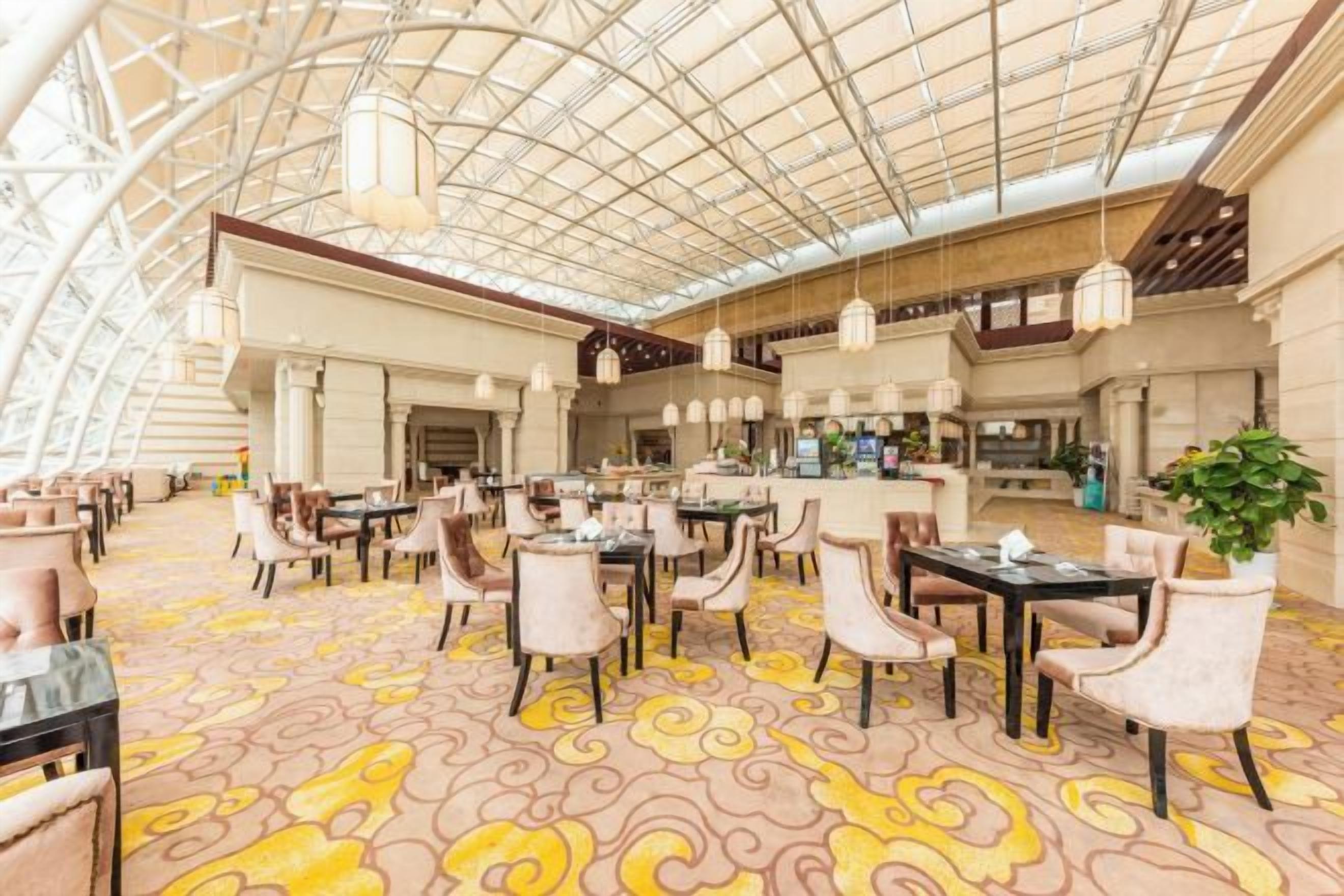 A spacious indoor area with tables and chairs, a high ceiling with a grid pattern, and a patterned carpet.