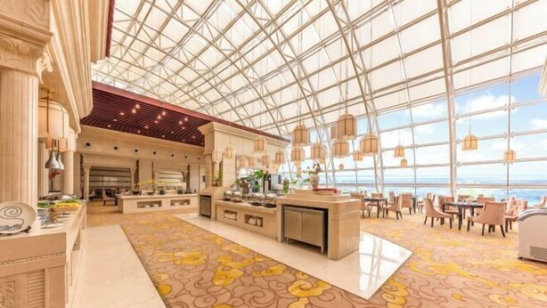 A spacious hotel lobby with a high ceiling, large windows, and a patterned carpet.
