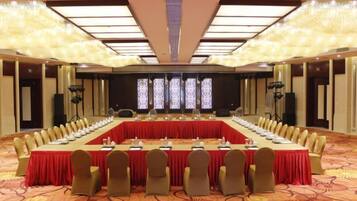A conference room with a long table, chairs, and a stage with a screen.