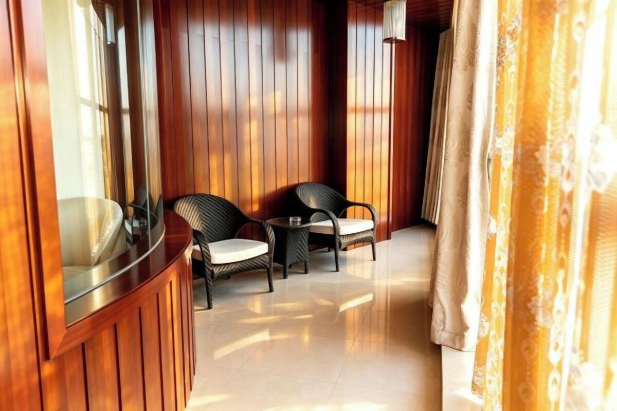 A corridor with wooden walls and a curved glass window, leading to a seating area with two wicker chairs.
