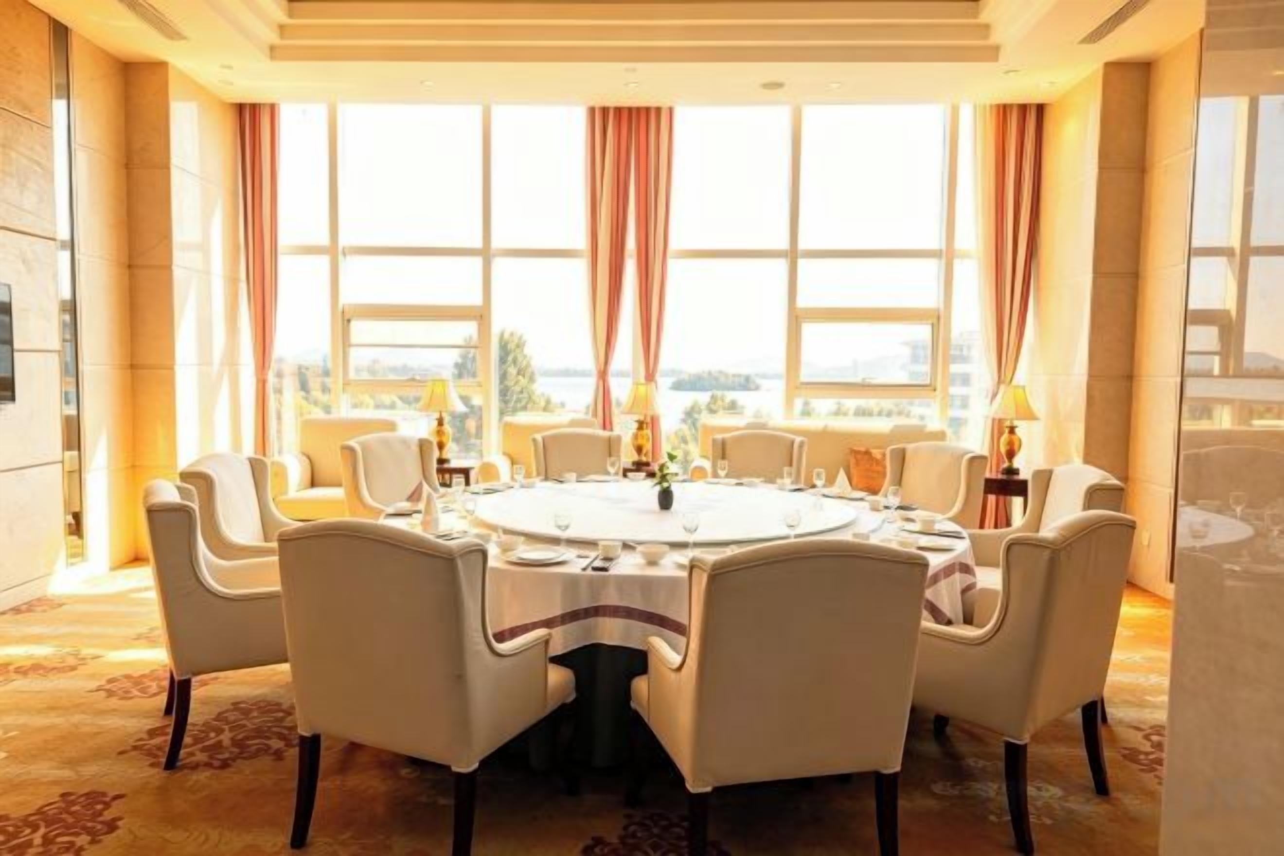 A round dining table with eight chairs, large windows with curtains, and a view of the cityscape.