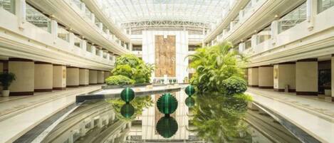 A spacious atrium with a glass ceiling, a central reflective pool, and symmetrical landscaping.
