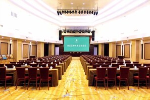A conference room with rows of chairs facing a large screen, a stage with a podium, and a carpeted floor. - Wei Select Xueye Hotel (Jinan)