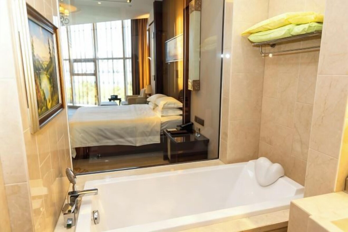 A hotel room with a large bed, a bathtub, and a view of the outdoors.