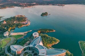 Vista aérea de una zona costera con arquitectura moderna, incluyendo un edificio curvo con fachada de vidrio y una estructura en forma de cúpula, rodeado de agua y vegetación.