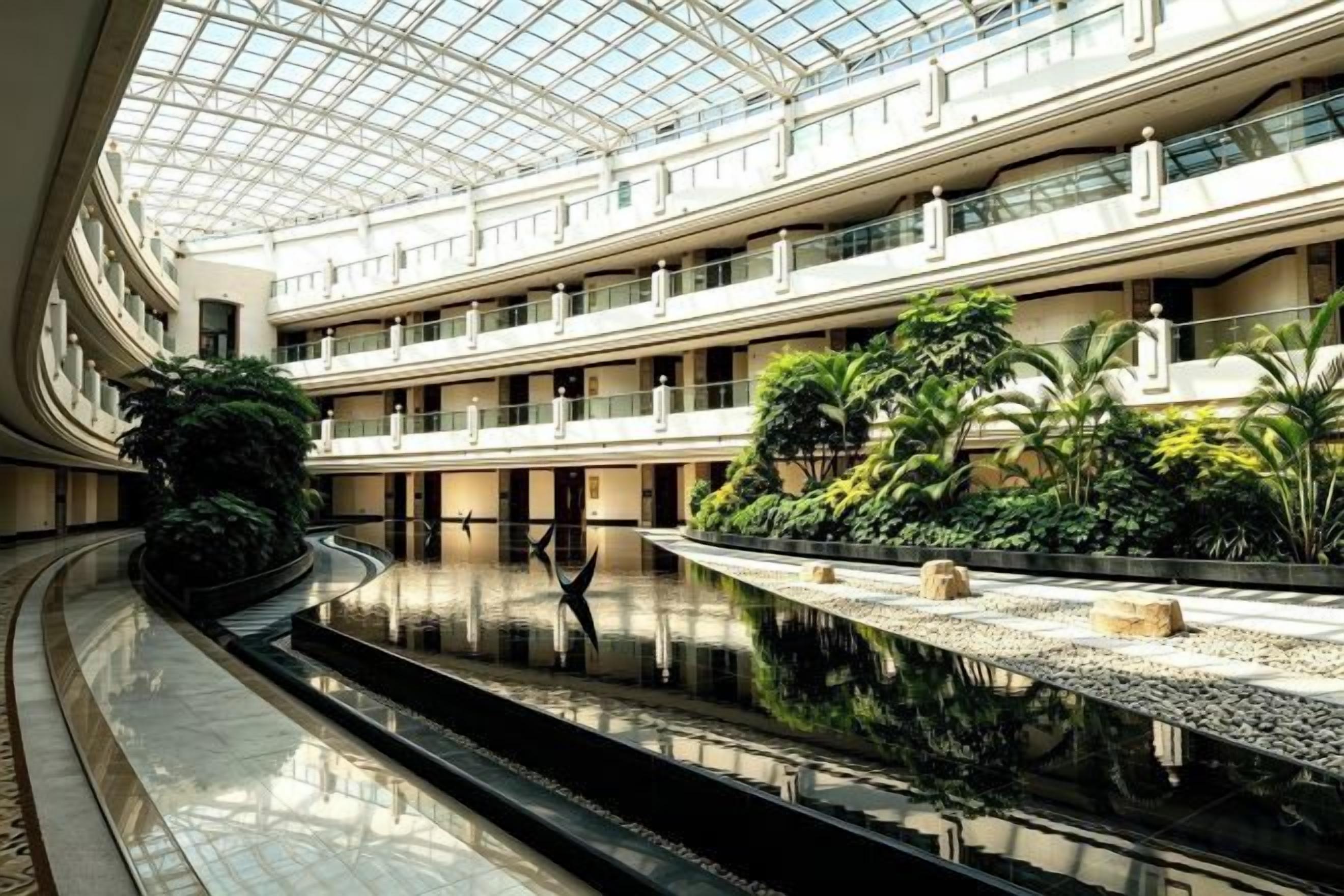 Een atrium met meerdere niveaus, een centraal waterbassin, balkons en beplanting.