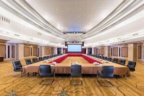 Een vergaderzaal met een lange tafel, stoelen, een projectiescherm en een vloerbedekking.