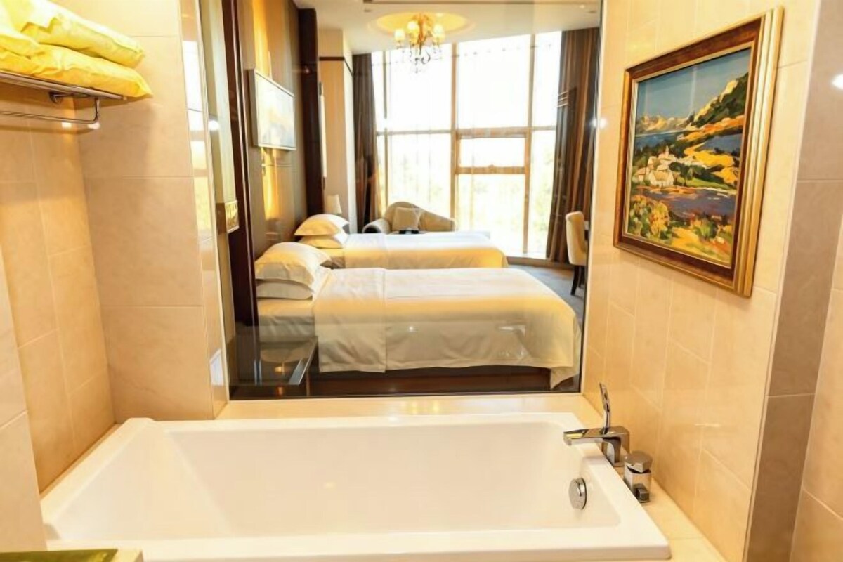 A hotel room with a large bathtub, two beds, a painting on the wall, and a view through a glass door.