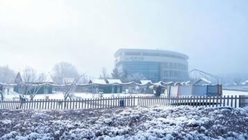 A building with a circular structure, a fenced area with snow-covered bushes, and a clear sky.