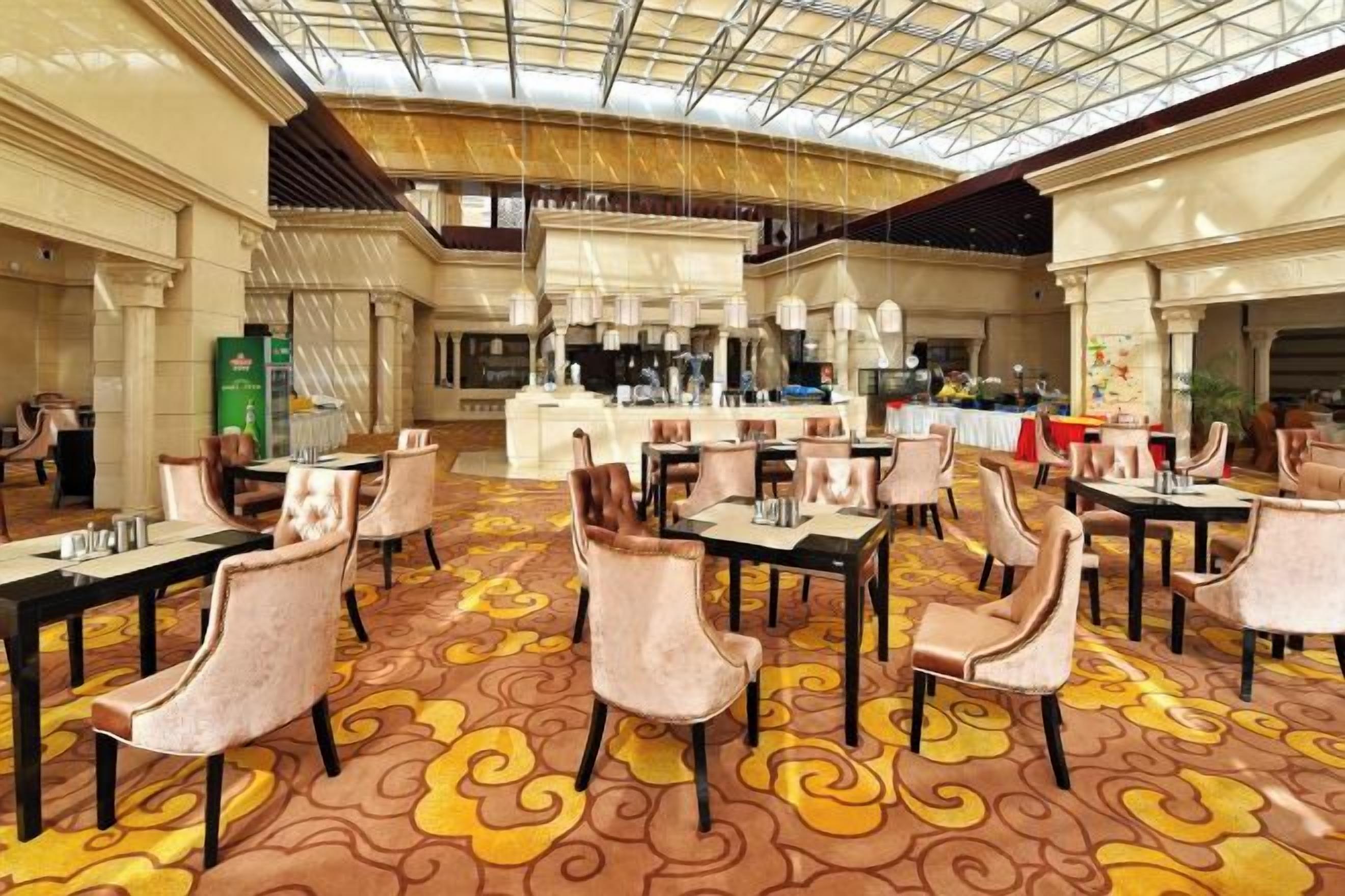 A spacious dining area with multiple tables and chairs, a central bar, and a high ceiling with a glass structure.