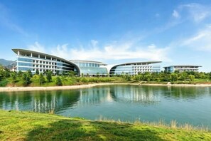 A modern building with a curved facade, a body of water in the foreground, and a clear sky. - Wei Select Xueye Hotel (Jinan)