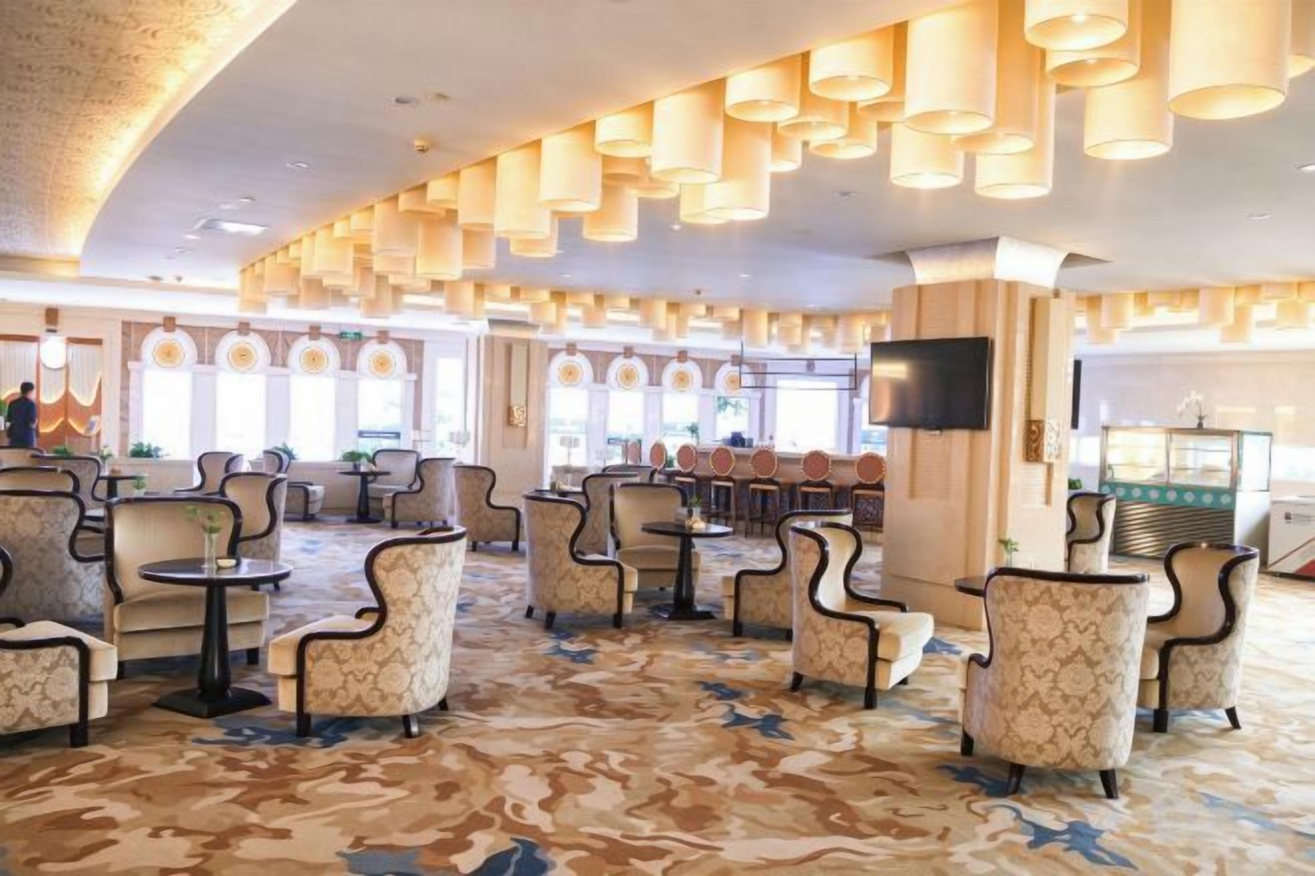 A spacious lobby with multiple seating areas, a television screen, and a bar area.