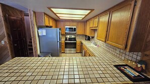 A kitchen with wooden cabinets, a refrigerator, a microwave, and a tiled floor. - Lakeside Condo at Donner Lake - 2 Bdrm. 2 Bath - 1st floor - steps from the lake (Truckee)