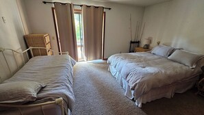 A bedroom with two beds, a wicker chair, a nightstand with a lamp, and a window with curtains. - Lakeside Condo at Donner Lake - 2 Bdrm. 2 Bath - 1st floor - steps from the lake (Truckee)