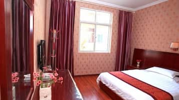 Una habitación de hotel con cama, mesita de noche, espejo, ventana con cortinas y suelo de madera.