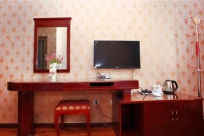 A hotel room with a wooden desk, a television, a mirror, a small stool, and a decorative vase. - Tiancheng Hotel (Dali City)