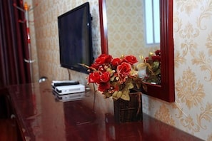 Una mesa de madera con un jarrón de rosas rojas, un televisor y un espejo decorativo.
