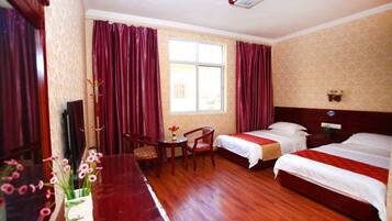 A hotel room with two beds, a desk, a chair, a window with curtains, and a wall-mounted decoration.