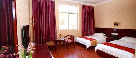 A hotel room with two beds, a desk, a chair, a window with curtains, and a wall-mounted decoration.