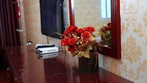 A room with a wooden table, a television, and a vase with red flowers. - Tiancheng Hotel (Dali City)