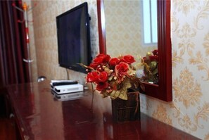 A room with a wooden table, a television, and a vase with red flowers. - Tiancheng Hotel (Dali City)