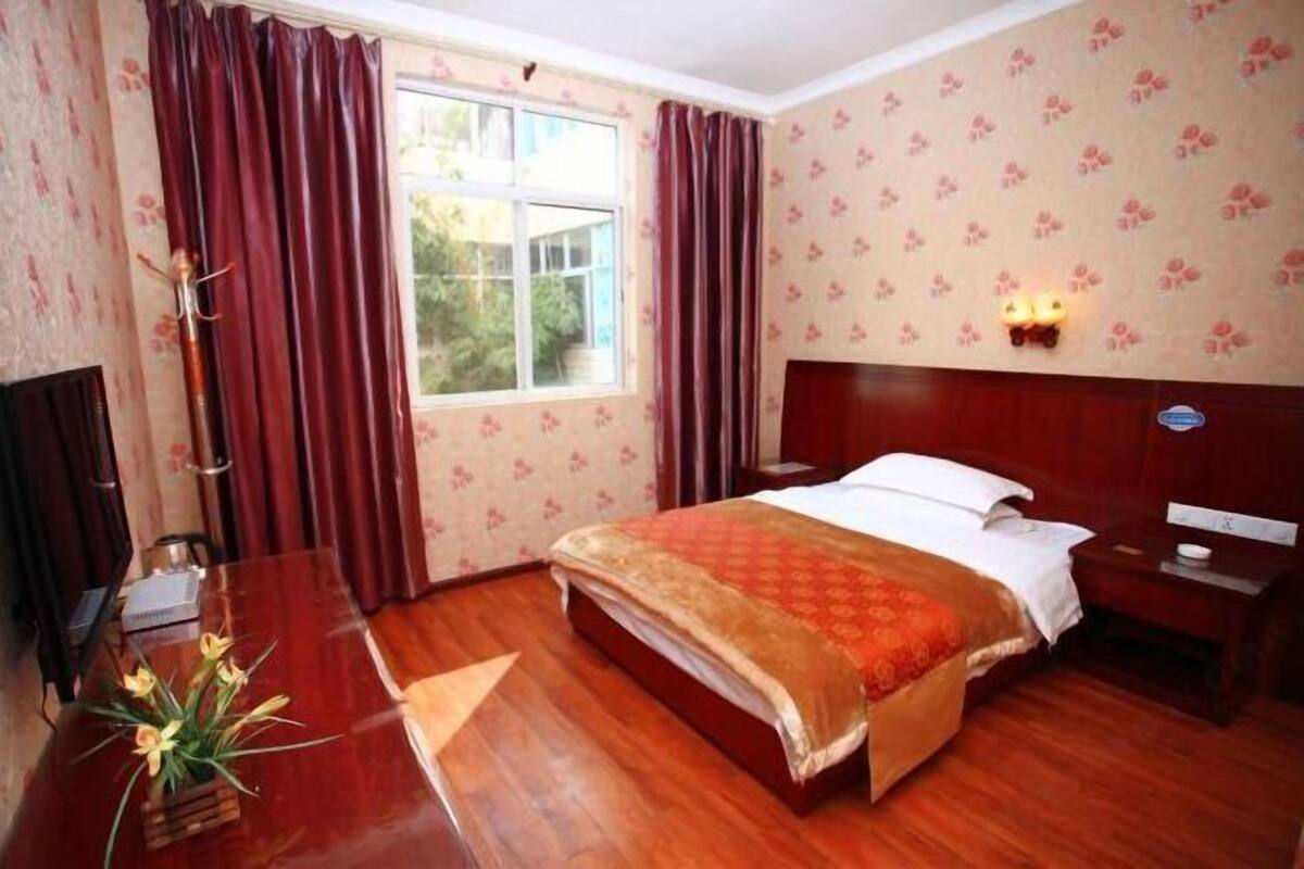 A hotel room with a wooden bed, a desk, a chair, a TV, and a window with curtains.