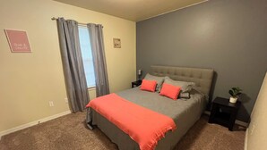 Ein Schlafzimmer mit Bett, Vorhängen, einem Nachttisch und einem an der Wand hängenden Bild.