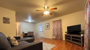 Ein Wohnzimmer mit einer Couch, einem Fernseher, einem Deckenventilator und einem Essbereich im Hintergrund.